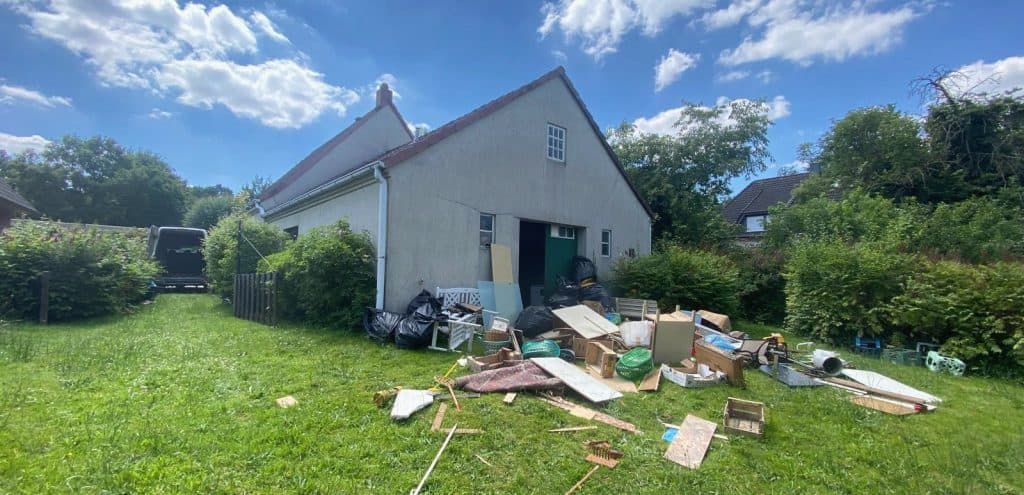 Ausgeräumte Möbel, Kartons und Säcke auf der Wiese vor einem Haus