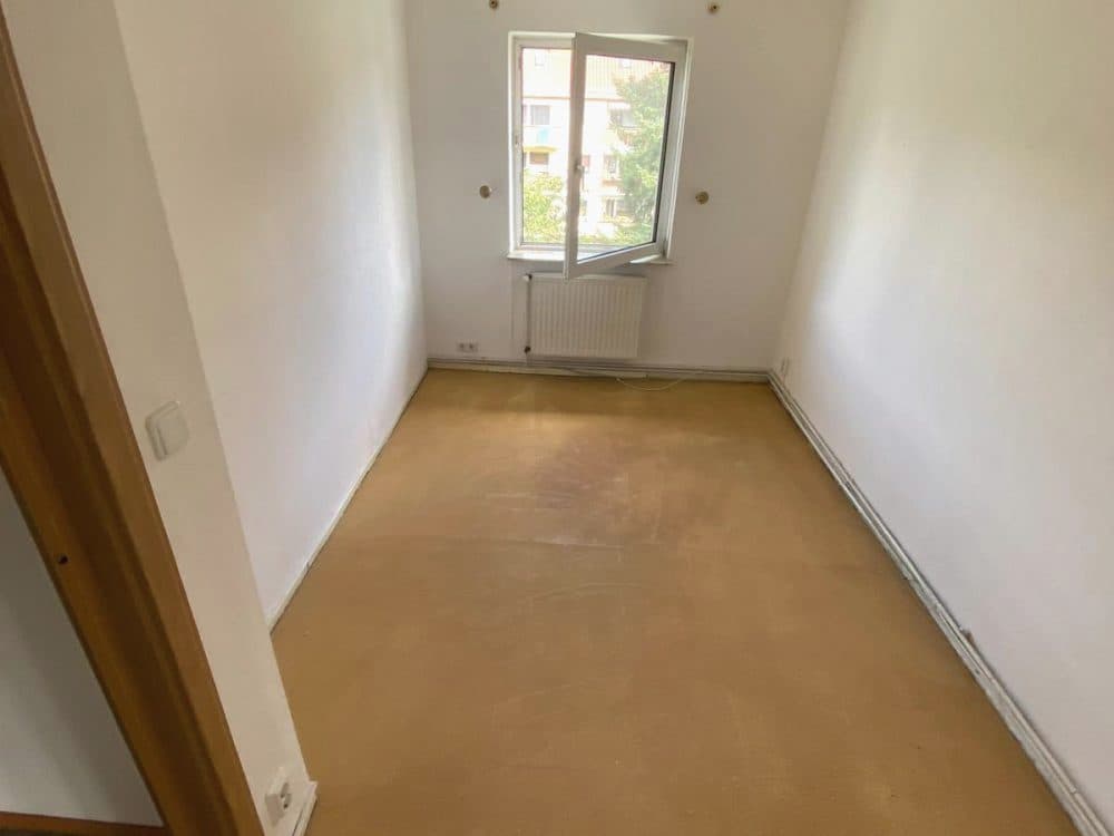 Leeres, schmales Zimmer mit Fenster und hellem Boden