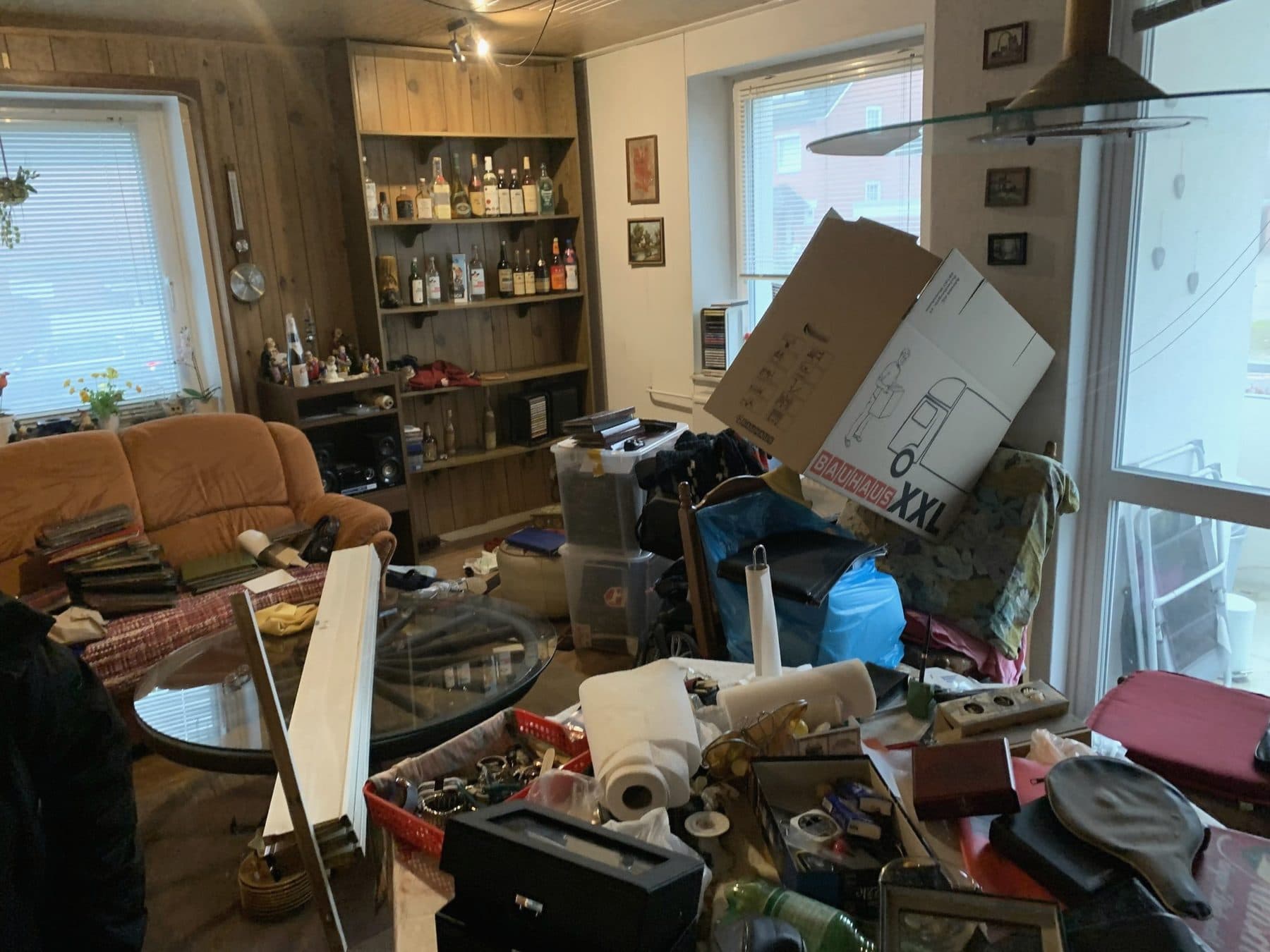Wohnzimmer vor der Räumung: Sofa, Regale, Kartons und Hausrat