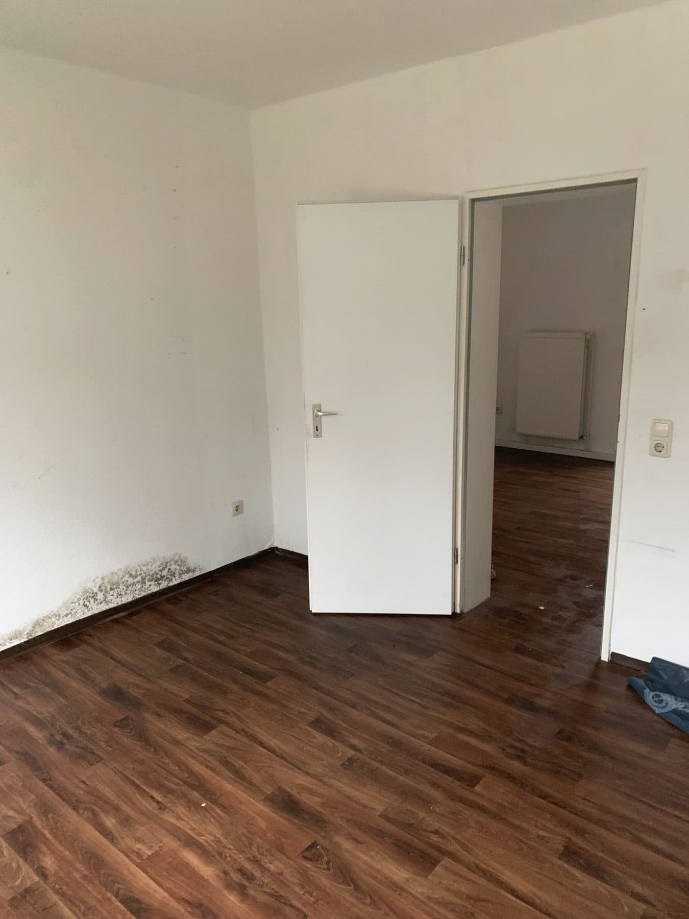 Leerer Raum mit dunklem Holzboden und offener Tür nach einer Räumung