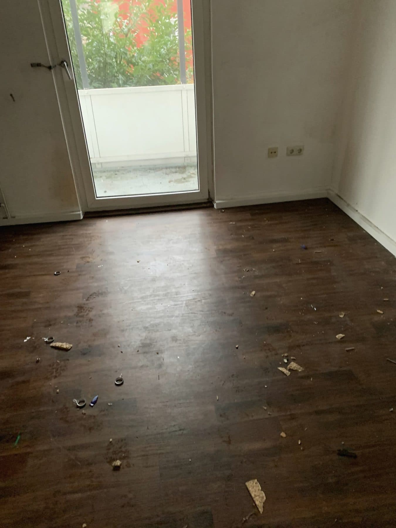 Leer geräumtes Zimmer mit dunklem Holzboden und Balkontür, einzelne Reste auf dem Boden